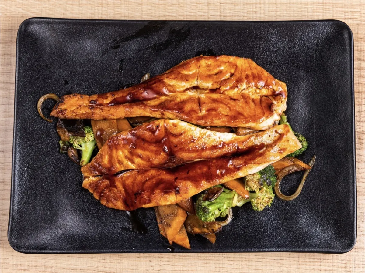 Two glazed hibachi salmon fillets plated over grilled broccoli, carrot, onion and mushroom