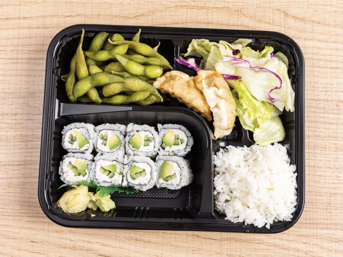Lunch bento box holding a California roll, edamame, gyoza, house salad and white rice in a divided tray