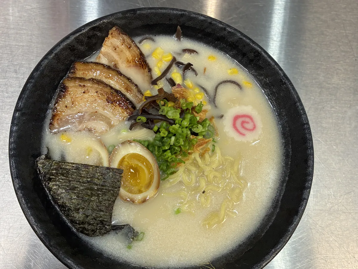 Bowl of tonkotsu ramen with chashu pork, a soft marinated egg, corn, wood ear mushroom, narutomaki and nori