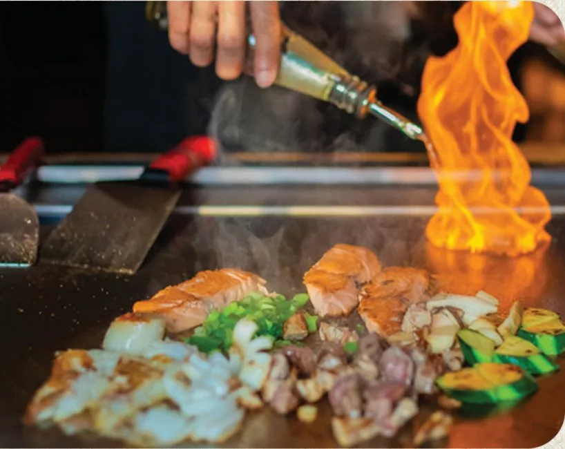 Chef searing hibachi salmon, steak and vegetables on the flat-top grill